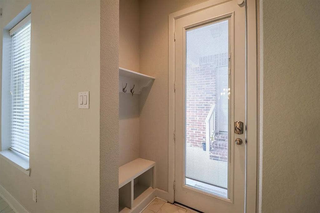 Built-in entryway storage featuring a bench seat, shelving, and double hooks, paired with a full-lite glass door