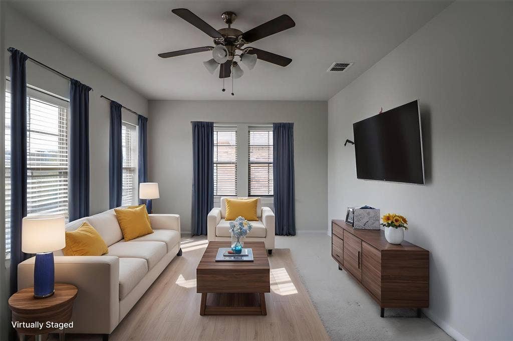 Living area featuring wood-finish flooring, a neutral color palette, multiple windows with blinds, and a multi-blade ceiling fan with integrated lighting