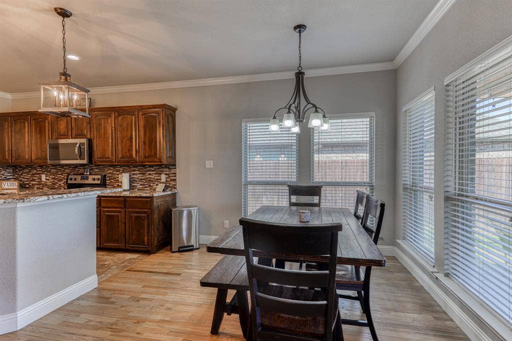 128 Breeders Drive, Willow Park, TX 76087 Kitchen featuring stained wood cabinetry, stone-patterned backsplash, wood-finish flooring, crown molding, and two distinct overhead pendant light fixtures