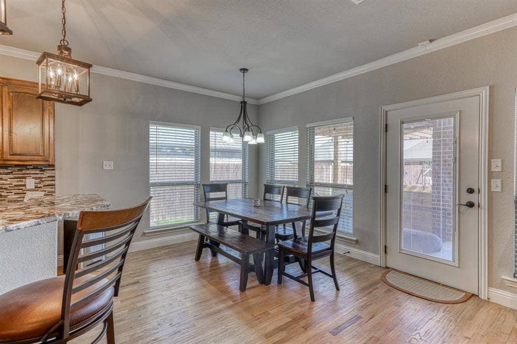 128 Breeders Drive, Willow Park, TX 76087 Dining area featuring wood-finish flooring, multi-pane windows with integrated blinds, crown molding, and a decorative pendant light fixture