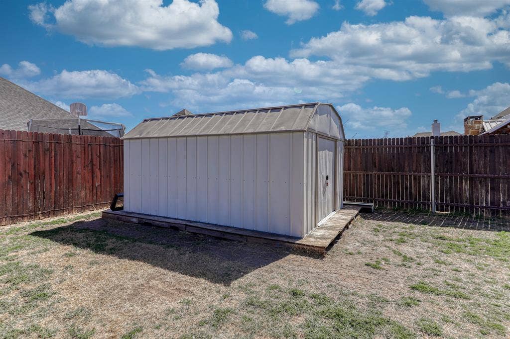 128 Breeders Drive, Willow Park, TX 76087 Detached metal storage shed featuring a gambrel roof and foundation-mounted platform, enclosed by a full-perimeter wood privacy fence