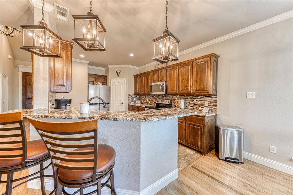 128 Breeders Drive, Willow Park, TX 76087 Kitchen featuring stained wood cabinetry, multi-tonal backsplash tile, stone-finish countertops, and hanging geometric lantern lighting