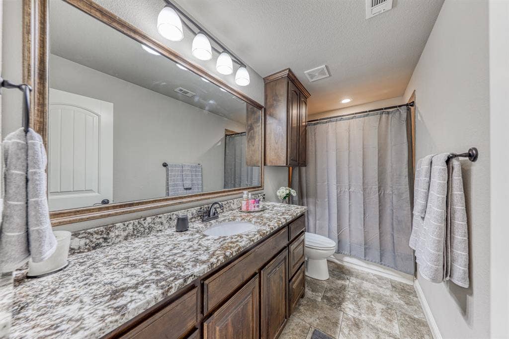 128 Breeders Drive, Willow Park, TX 76087 Bathroom featuring a stone-patterned countertop, dark wood-finish cabinetry, an expansive wall-mounted mirror, four-light vanity fixture, and tiled flooring