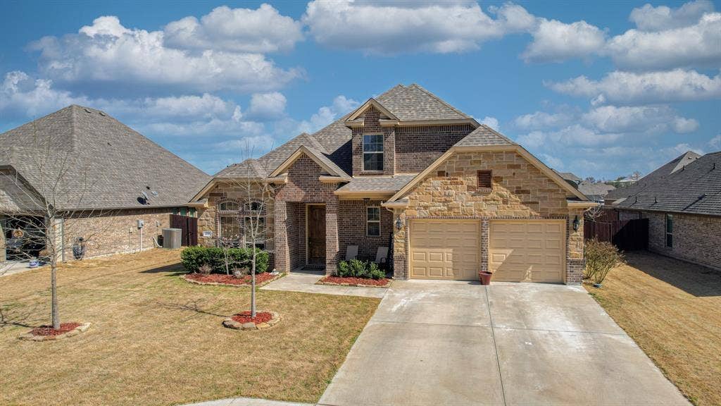 128 Breeders Drive, Willow Park, TX 76087 Multi-gabled brick and stone exterior featuring a two-car garage, steep shingled rooflines, and a concrete driveway