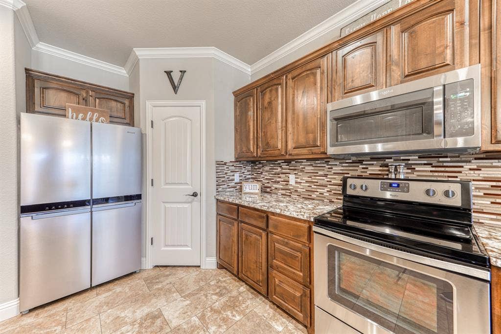 128 Breeders Drive, Willow Park, TX 76087 Kitchen featuring stained wood cabinetry, multi-tonal mosaic tile backsplash, stone-surface countertops, and stainless steel appliances