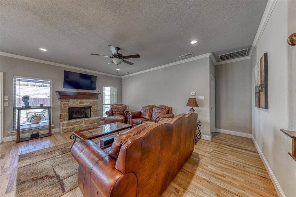 128 Breeders Drive, Willow Park, TX 76087 Living area featuring wood-finish flooring, a stone-faced fireplace with a timber mantel, crown molding, and recessed lighting