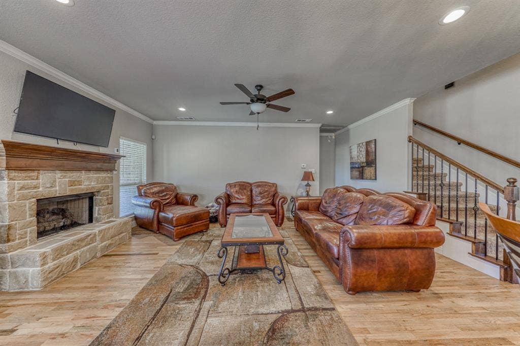128 Breeders Drive, Willow Park, TX 76087 Stone-faced fireplace with a wood mantel, wood-finish flooring, recessed lighting, ceiling fan, and staircase with a wood handrail and metal balusters