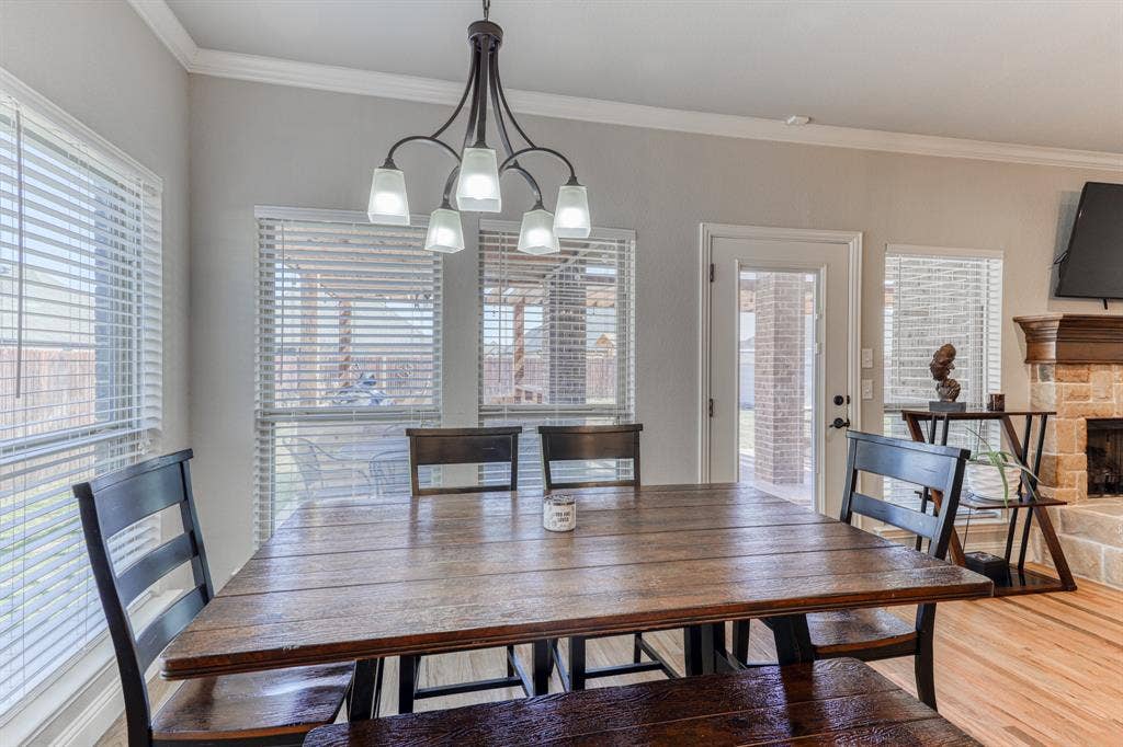 128 Breeders Drive, Willow Park, TX 76087 Dining area featuring multi-light metal chandelier, windows with horizontal blinds, glass-panel exterior door, and stone-surround fireplace with wood mantel