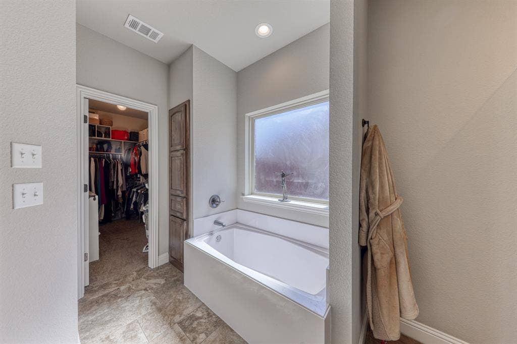 128 Breeders Drive, Willow Park, TX 76087 Deep soaking tub with a metal faucet, tile flooring, built-in wooden cabinetry, recessed ceiling lighting, and a privacy window