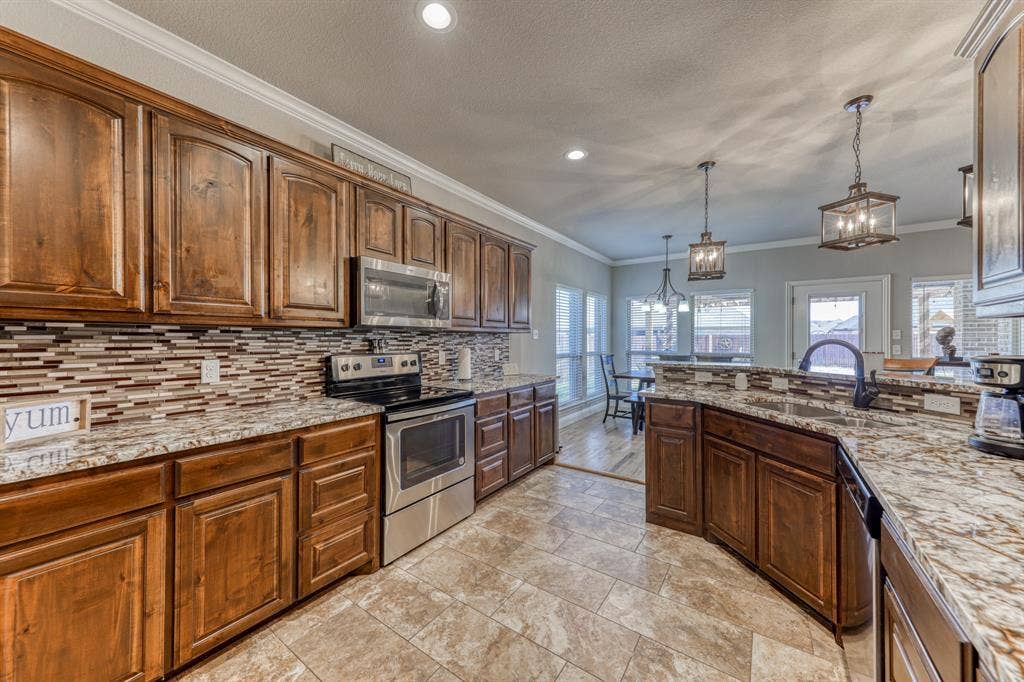 128 Breeders Drive, Willow Park, TX 76087 Kitchen featuring stained wood cabinetry, patterned stone-surface countertops, horizontal multi-tone tile backsplash, stainless steel appliances, and tile flooring