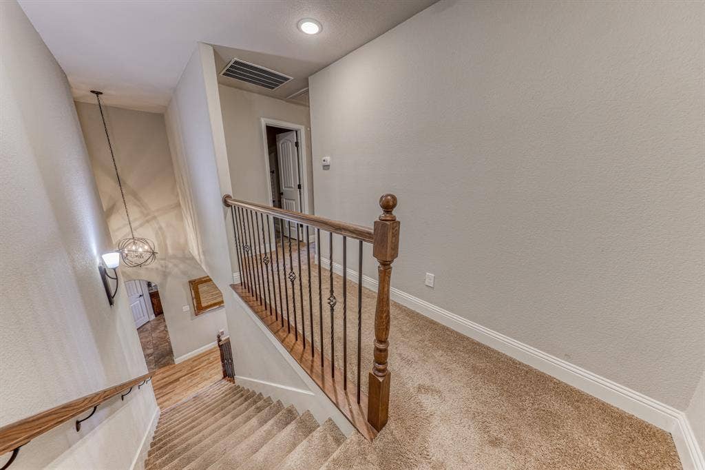 128 Breeders Drive, Willow Park, TX 76087 Carpeted hallway featuring a wood and metal balustrade, recessed ceiling lighting, and a multi-light spherical chandelier