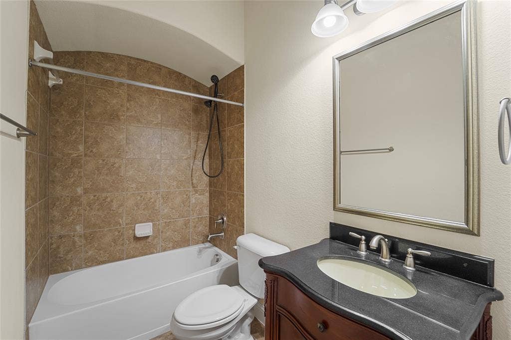 Bathroom featuring a vanity with dark stone countertop, an arched shower enclosure with tiled surround, a porcelain tub, and a framed wall mirror with integrated lighting
