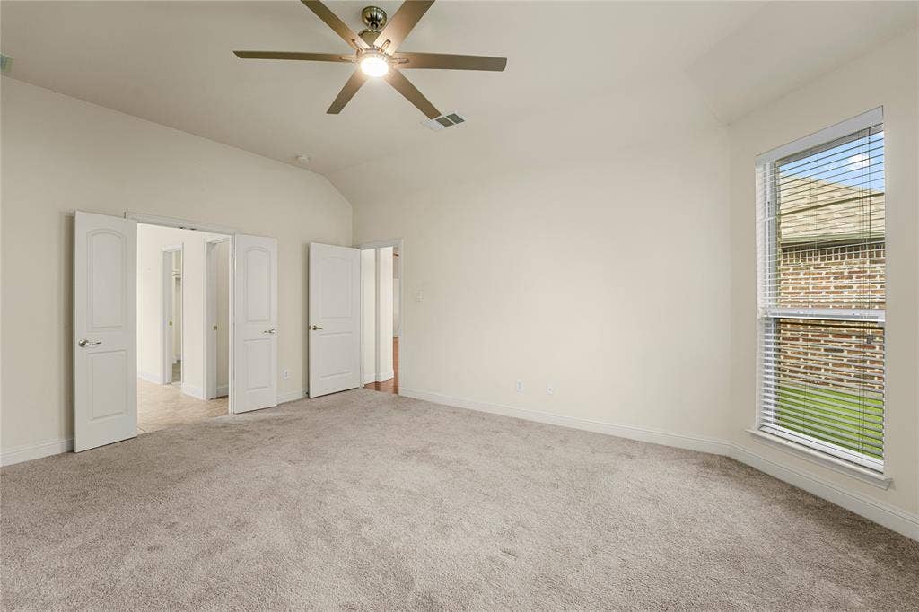 Vaulted ceilings, neutral wall color, wall-to-wall carpeting, ceiling fan with light fixture, and large windows with horizontal blinds