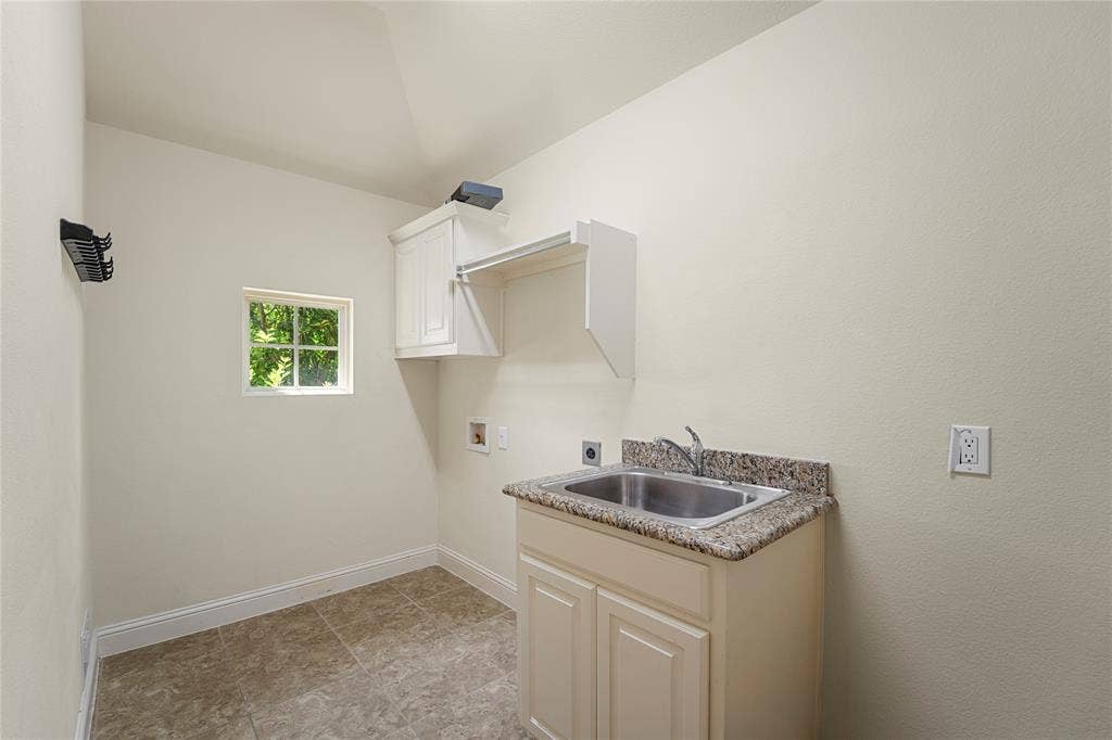 Utility room featuring stone-finish countertop with drop-in stainless steel sink, built-in cabinetry, overhead shelving, and tile flooring