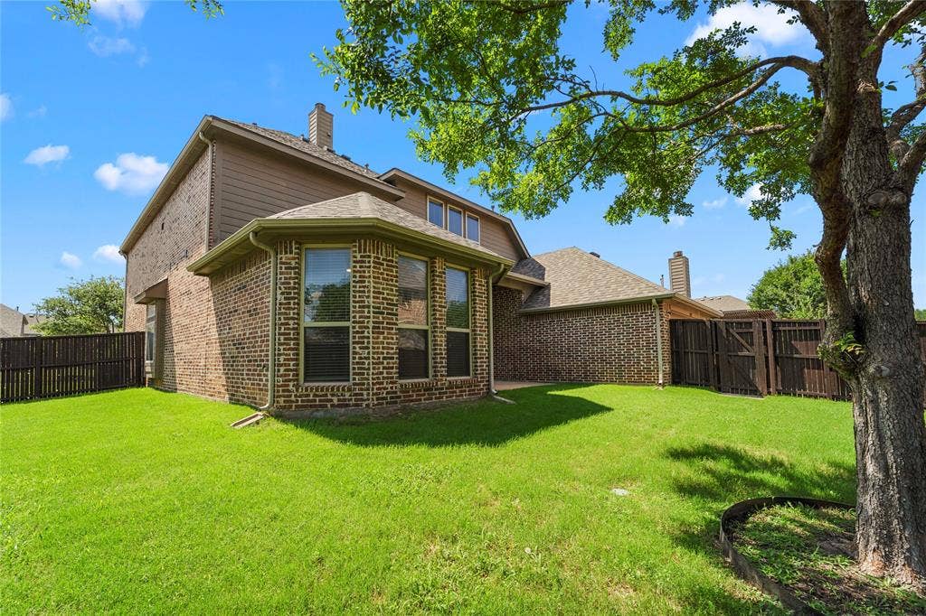 Exterior rear elevation featuring brick siding, a bay window configuration, multi-level roof lines, and a fenced backyard with mature trees