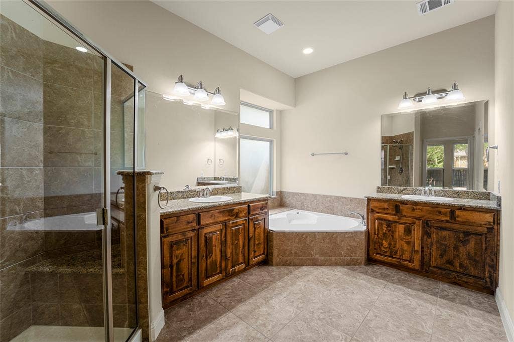 Dual vanity with stone-surfaced countertops, corner soaking tub, and glass-enclosed shower with tiled surround