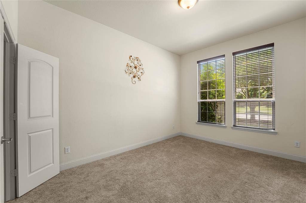 Neutral-toned room featuring plush wall-to-wall carpeting, dual windows with integrated blinds, and a solid-core interior door