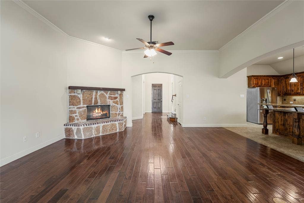 Living area featuring wood-finish flooring, a corner masonry fireplace with a wood mantel, an arched entry, and a ceiling fan