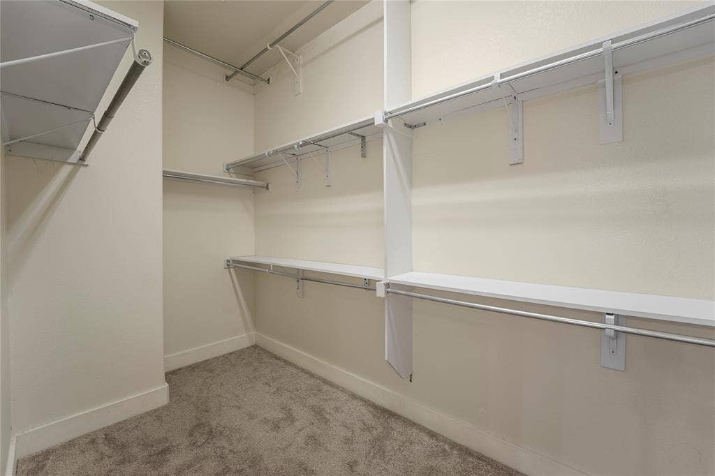 Walk-in storage space featuring multi-level white shelving and integrated metal hanging rods