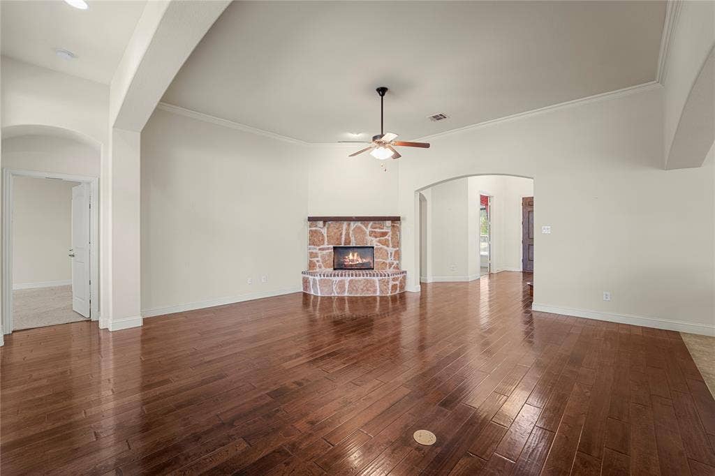 Living area featuring high ceilings, wood-finish flooring, corner stone fireplace with a timber mantel, and a ceiling fan