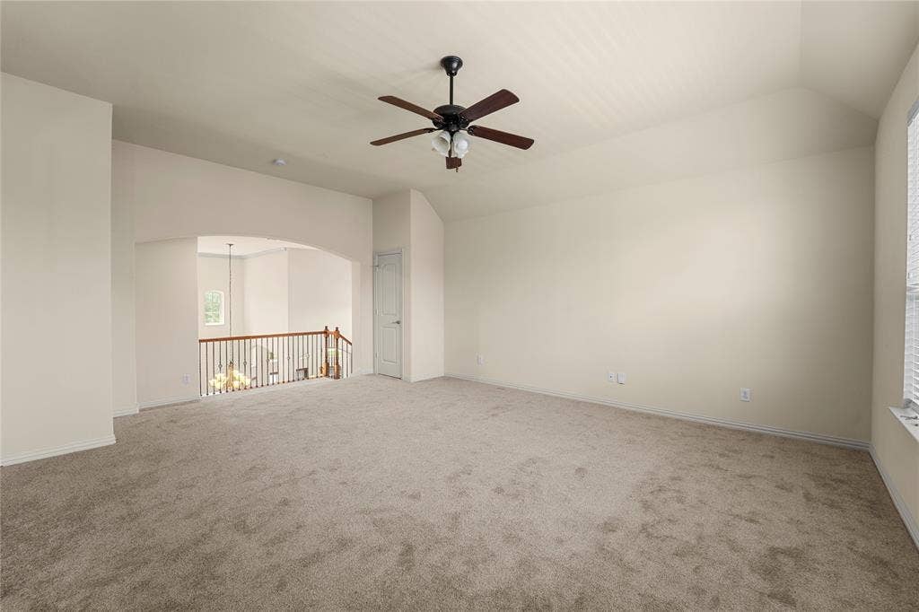 Vaulted ceiling, carpeted flooring, centrally mounted ceiling fan with integrated lighting, and wooden baluster railing