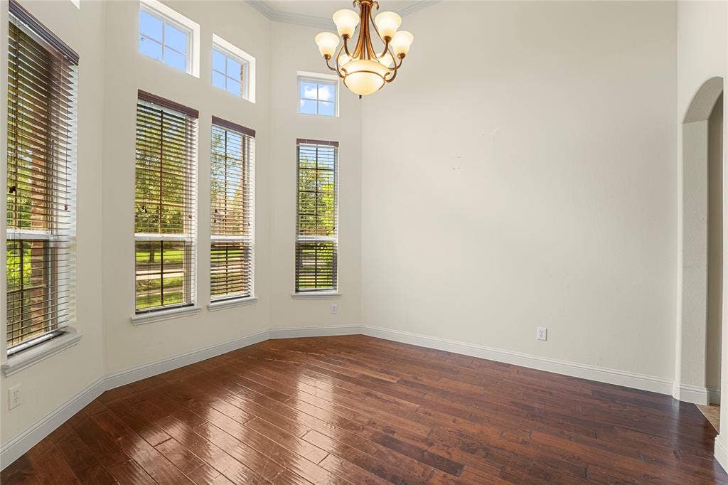 Multi-windowed space featuring wood-finish flooring, high ceilings, arched architectural detailing, and a multi-arm chandelier