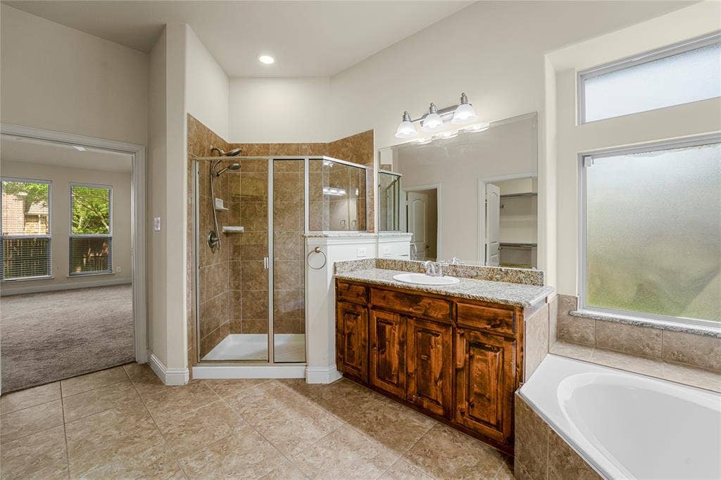 Bathroom featuring tile flooring, a walk-in shower with a glass enclosure, a dual-sink vanity with a countertop, and a built-in soaking tub