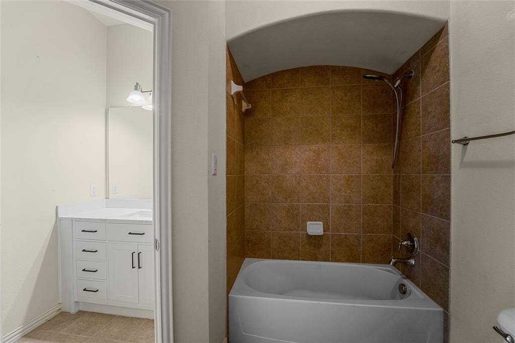 Bathroom featuring a bathtub with a tiled surround, arched ceiling detail, white vanity cabinetry with a rectangular sink, and a framed mirror