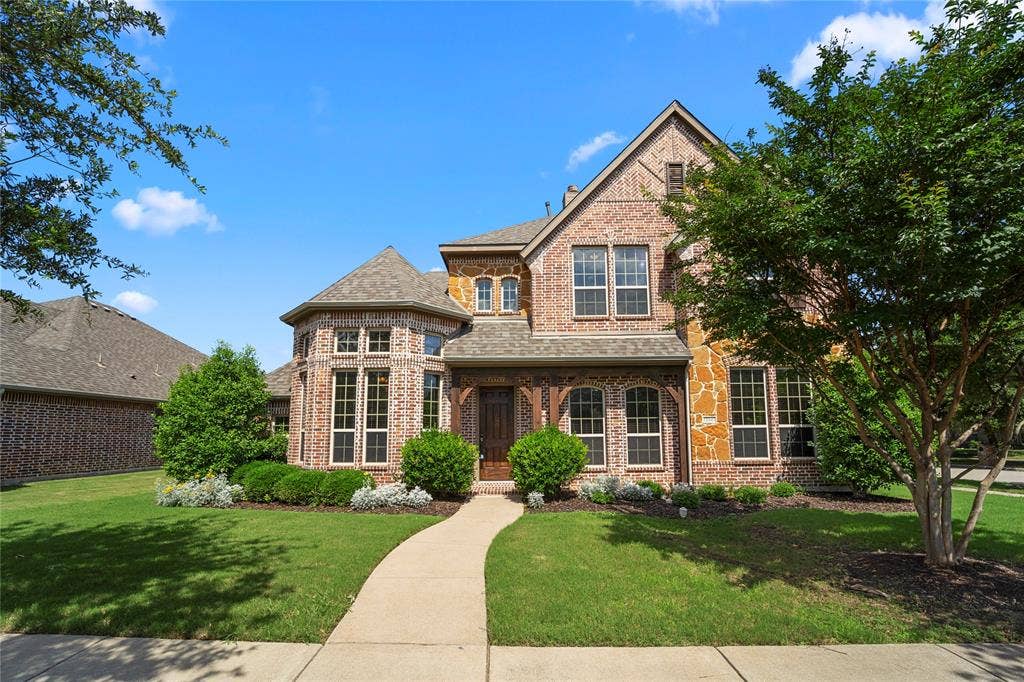 Multi-story residence featuring a combination of brick and natural stone masonry, a steeply pitched roofline with gables, turret-style architectural detailing, and a concrete walkway