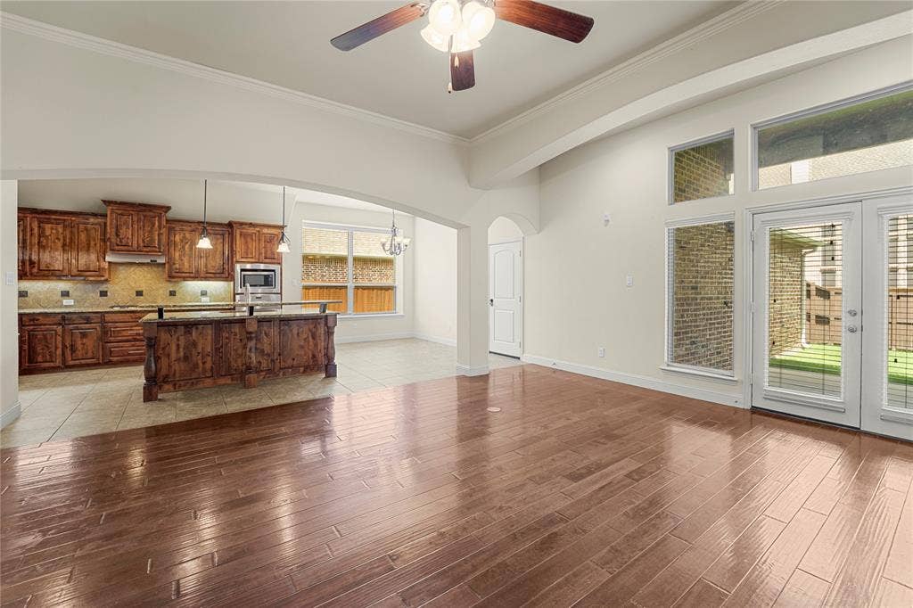 Open-concept space featuring wood-finish flooring, high ceilings with a crown molding detail, an arched room partition, expansive windows with transoms, and a kitchen equipped with raised-panel cabinetry and a stone-surface island