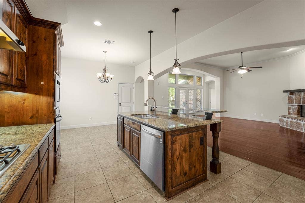 Kitchen featuring stained wood cabinetry, stone-surface countertops, central island with stainless steel appliances, dual-pendant lighting, and ceramic tile flooring
