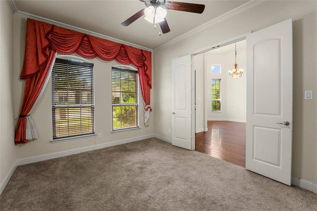 Room featuring carpeting, crown molding, double doors, and a ceiling fan with light fixture