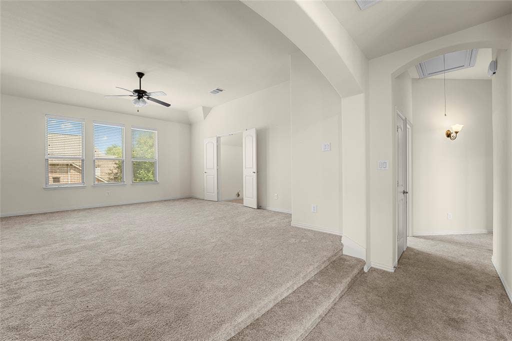 Sunken living area featuring neutral carpeting, high ceilings, multiple double-hung windows, a ceiling fan, and an arched entryway