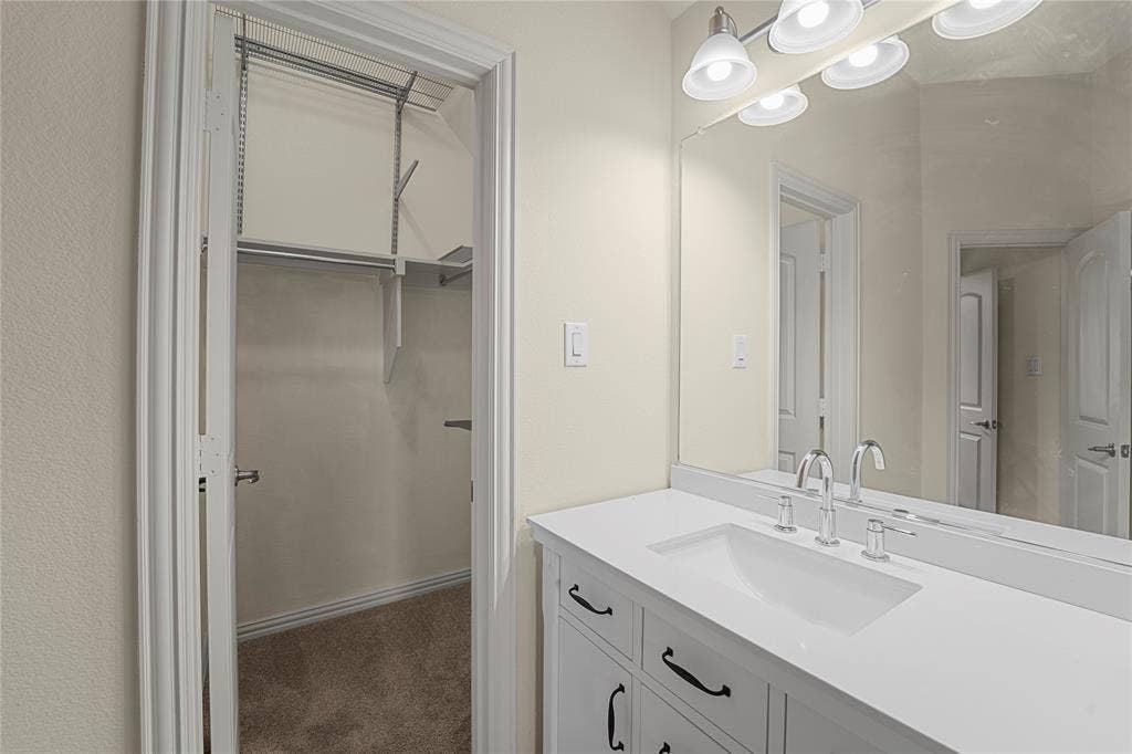 White vanity with stone-composite countertop, undermount sink, chrome fixtures, full-width vanity mirror, and built-in closet shelving