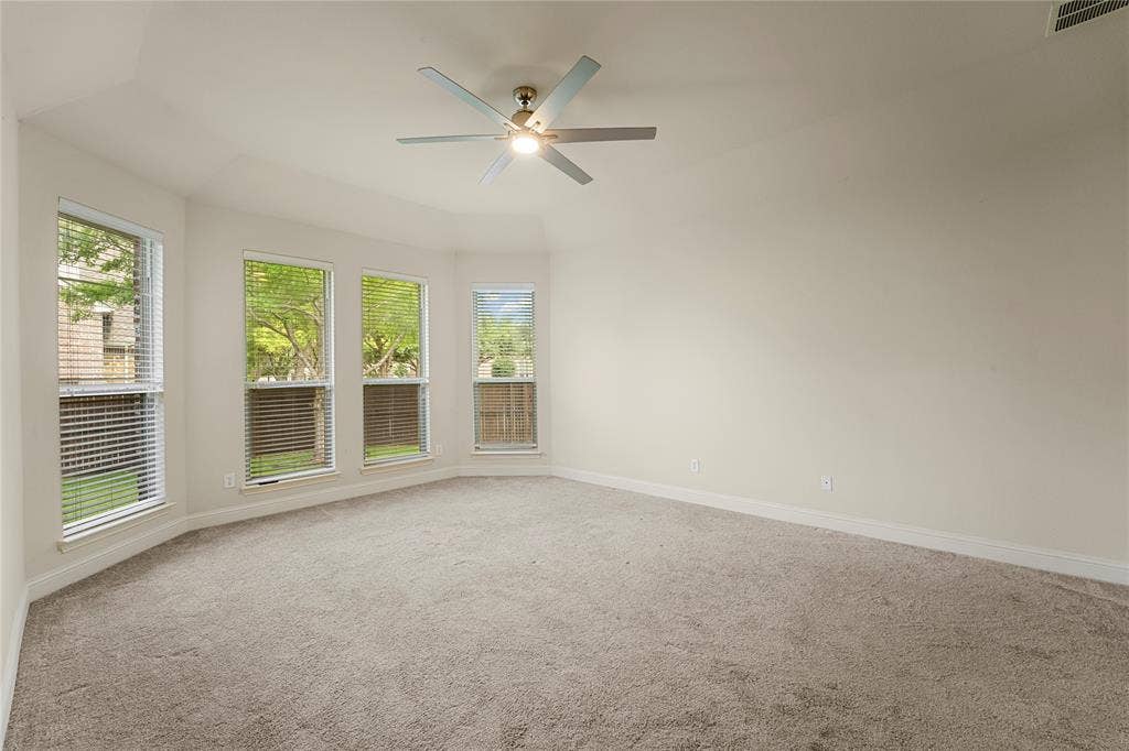 Neutral-toned interior featuring a vaulted ceiling, wall-to-wall carpeting, a multi-pane bay window assembly, and a ceiling-mounted fan with integrated lighting