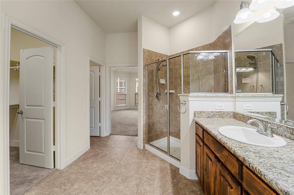 Bathroom featuring a walk-in shower with tile surround, stone-composite countertop with an integrated basin, stained wood cabinetry, and large-format tile flooring
