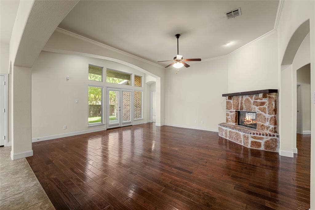 Spacious living area featuring wood-finish flooring, vaulted ceilings, a stone-accented fireplace with a wood mantel, and large windows with integrated glass doors