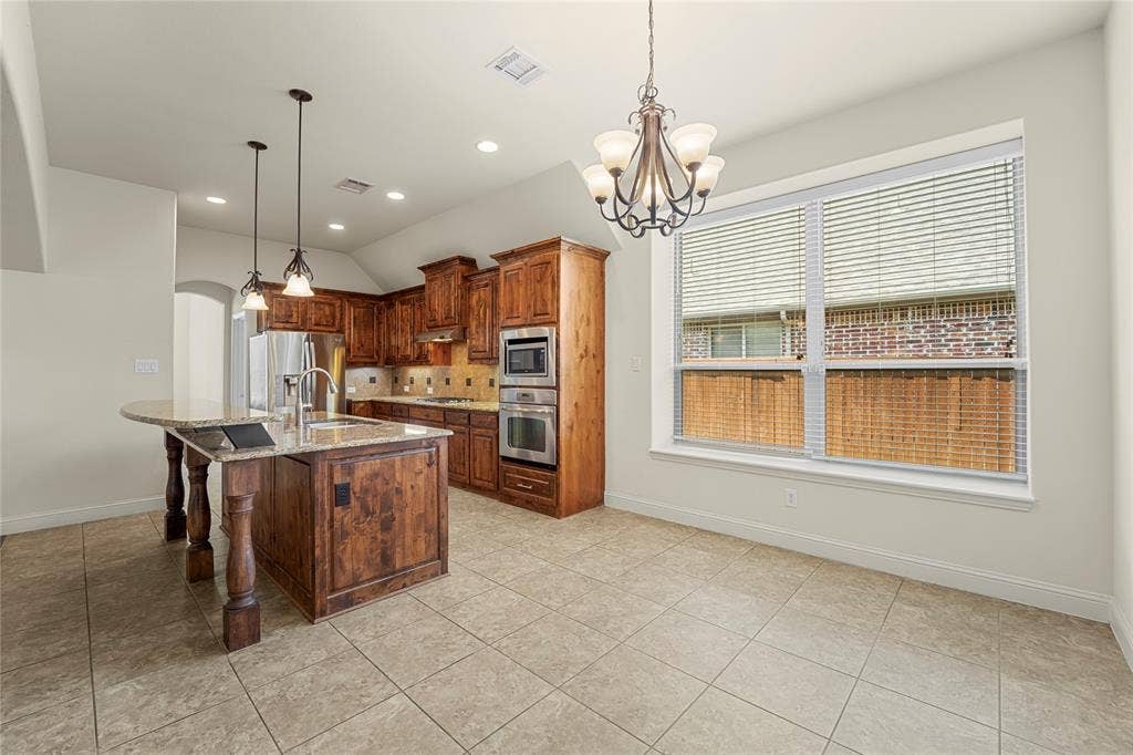 Kitchen featuring wood cabinetry, stone-surface countertops, tile flooring, built-in wall oven and microwave, and multi-light hanging fixtures