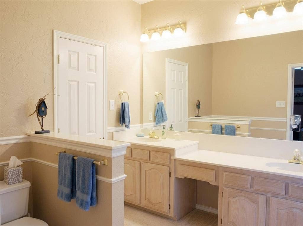 2306 Summit Drive, McKinney, TX 75071 Double-sink vanity with light-tone wood cabinetry, solid-surface countertop, full-width wall mirror, and integrated lighting fixtures