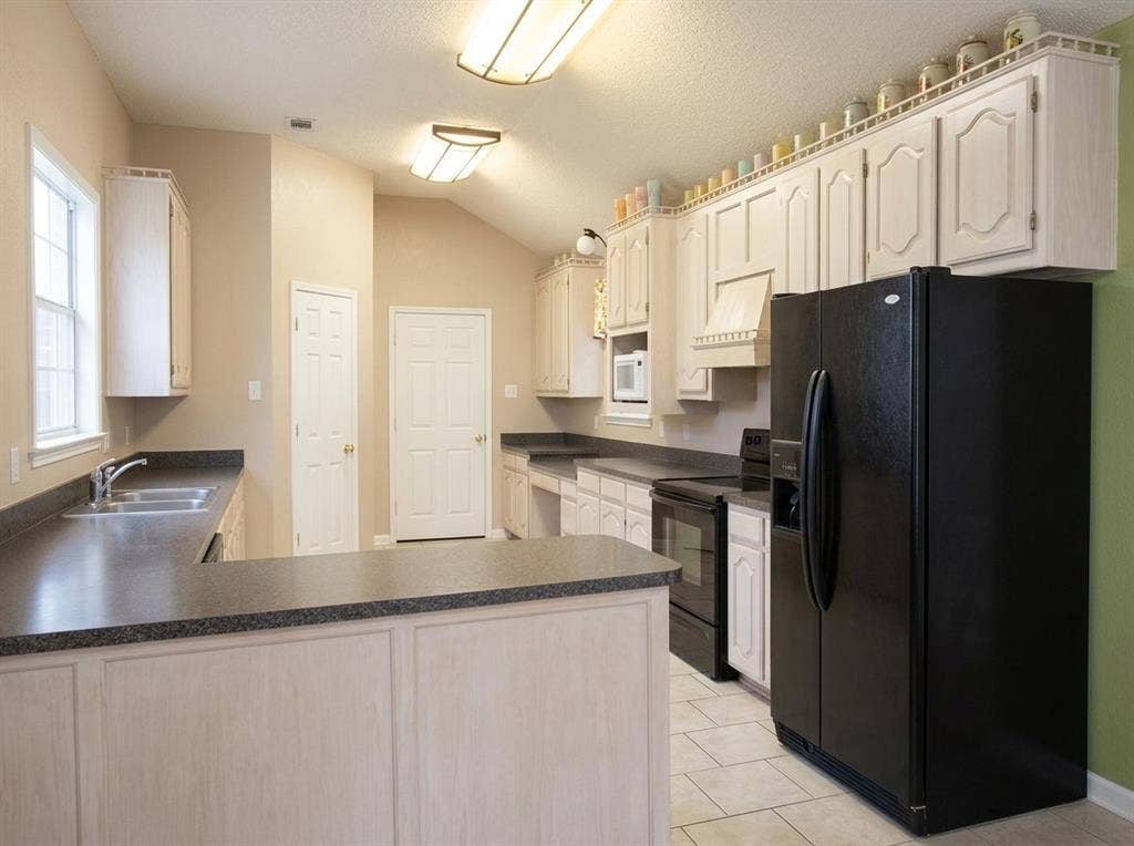 2306 Summit Drive, McKinney, TX 75071 Kitchen featuring light-toned cabinetry, dual-basin stainless steel sink, dark solid-surface countertops, vaulted ceiling, and tile flooring