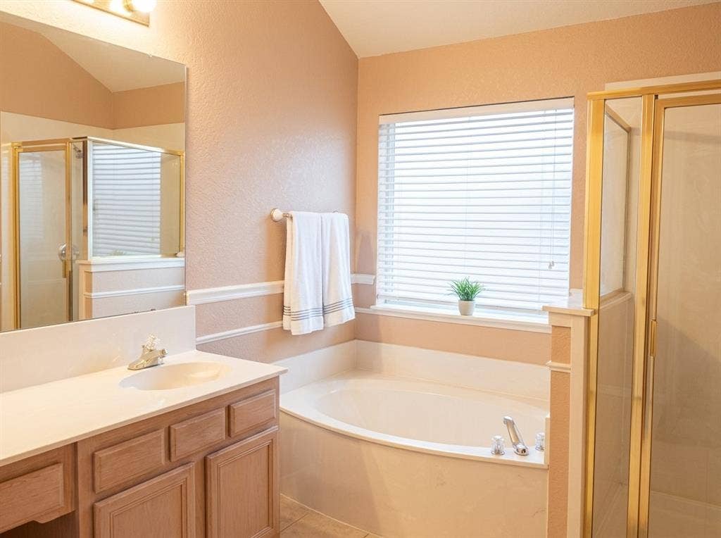 2306 Summit Drive, McKinney, TX 75071 Bathroom featuring a wood vanity with a solid-surface countertop, an integrated sink, a built-in soaking tub, a separate shower enclosure with a frame, and a large wall-mounted mirror