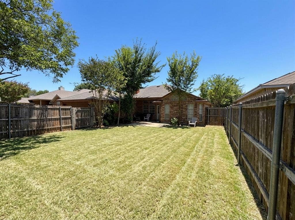 2306 Summit Drive, McKinney, TX 75071 Backyard featuring a manicured lawn, masonry exterior, concrete patio, wood-plank fencing, and mature trees