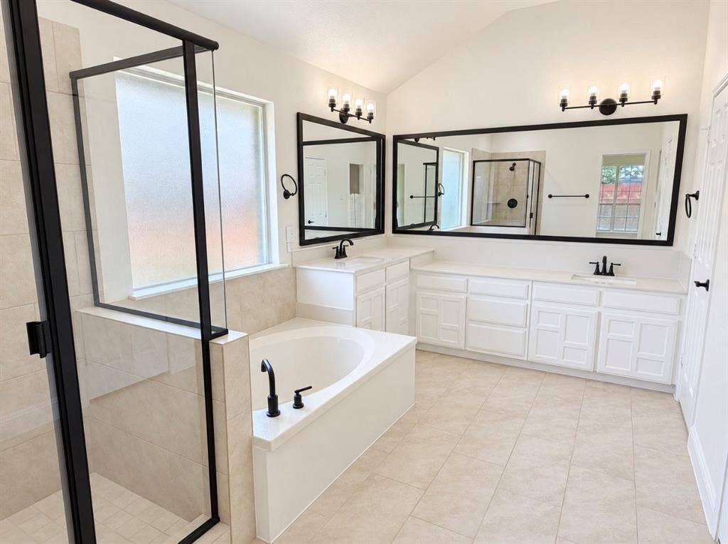 2400 Waterloo Lane, Mesquite, TX 75181 Bathroom featuring a double vanity with white cabinetry, a walk-in shower with a glass enclosure and matte black frame, a soaking tub with matte black hardware, dual framed mirrors, and tile flooring