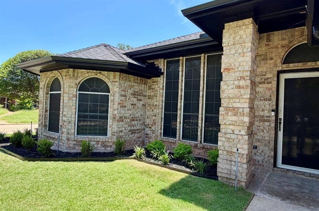 2400 Waterloo Lane, Mesquite, TX 75181 Exterior brick facade with stone-textured pillar, architectural roof shingles, arched windows, and dark metal trim framing