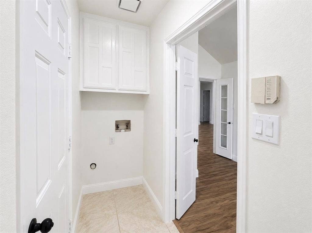 2400 Waterloo Lane, Mesquite, TX 75181 Utility area featuring white upper cabinetry, tiled flooring, wood-finish flooring in the exterior space, and multi-panel doors with matte black hardware