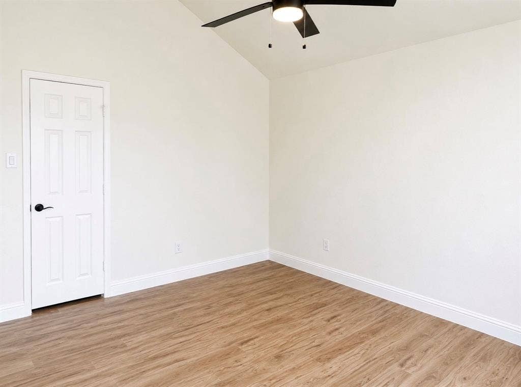 2400 Waterloo Lane, Mesquite, TX 75181 Vaulted ceiling featuring a central black ceiling fan with an integrated light fixture, complemented by wood-finish flooring and a white six-panel interior door with matte black hardware