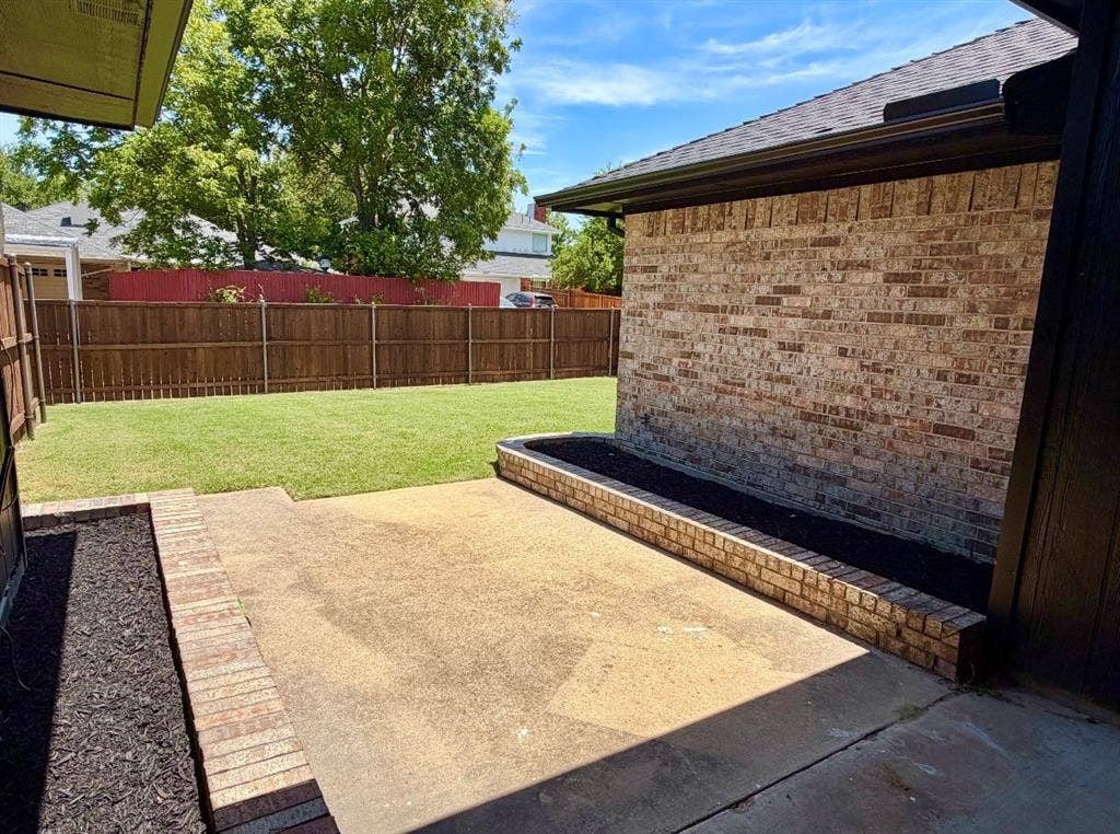 2400 Waterloo Lane, Mesquite, TX 75181 Concrete patio featuring brick-lined planting beds, brick exterior siding, and a wooden privacy fence surrounding a grass lawn