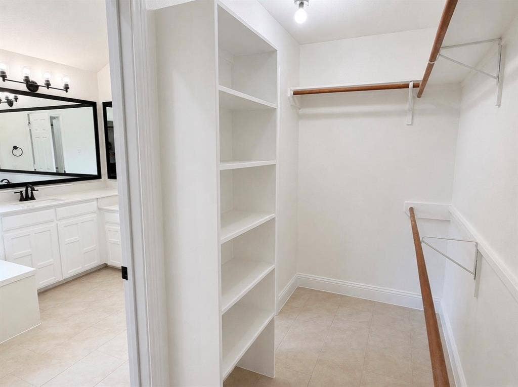 2400 Waterloo Lane, Mesquite, TX 75181 Walk-in closet featuring floor-to-ceiling built-in shelving and dual-tier wooden hanging rods, accompanied by a bathroom vanity with a black-framed mirror, white cabinetry, and matte black hardware