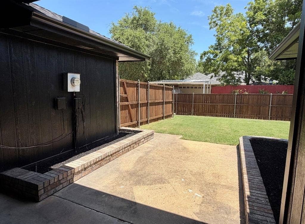 2400 Waterloo Lane, Mesquite, TX 75181 Concrete patio featuring dual raised brick planters, enclosed by a wood privacy fence and expansive lawn