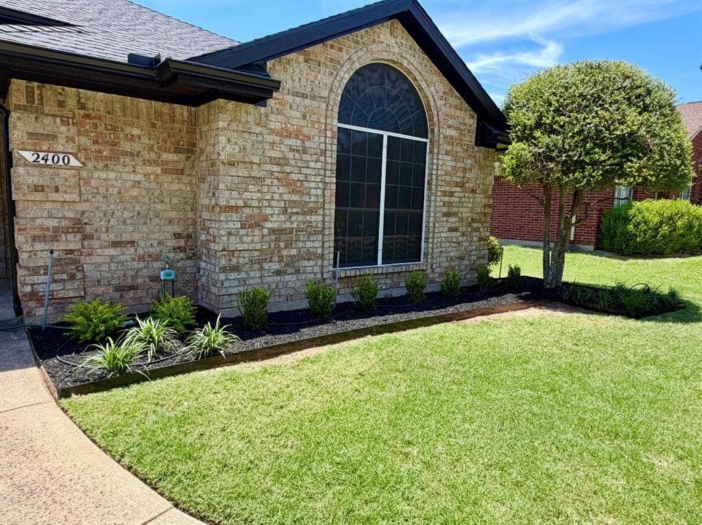 2400 Waterloo Lane, Mesquite, TX 75181 Brick exterior featuring a gabled roofline, arched window with decorative grille, and landscaped garden beds with dark mulch